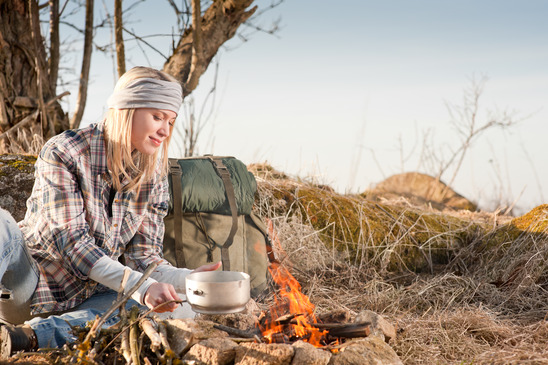 Hiking woman with backpack cook by campfire Young hiking woman with backpack cook on campfire in countryside